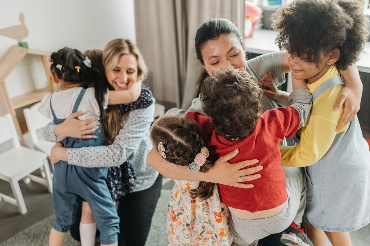 Two daycare teachers hug their young students in a warm, welcoming environment Two daycare teachers hug their young students in a warm, welcoming environment